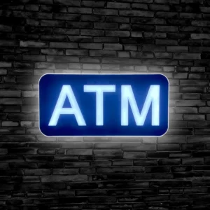 LED ATM Sign lit up against a black brick wall for retail businesses with ATMs.