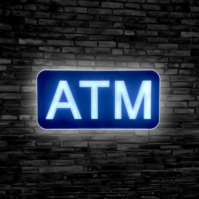 LED ATM Sign lit up against a black brick wall for retail businesses with ATMs.