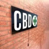 CBD LED sign with a green cross, hanging on a red brick wall