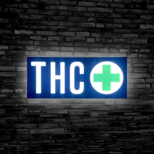 Lit up THC sign with green cross against a black brick wall