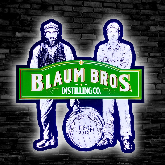 Blaum Bros Distilling Co Custom LED Sign of 2 men, 1 man with his leg up on a barrel, mounted on a black brick wall
