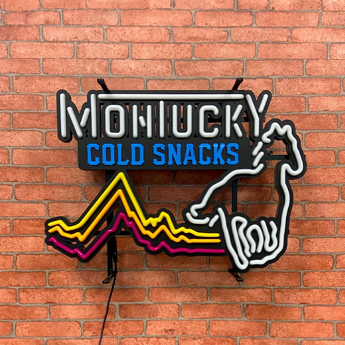 Neon sign on a brick wall that reads "montucky cold snacks" with a graphic of a hand holding a zigzagging mountain range, crafted by LEDON Signage.