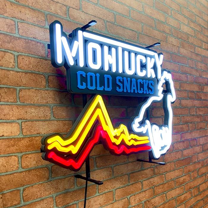LED neon sign on a brick wall reading "montucky cold snacks" with a colorful, neon outline of a mountain and a rearing horse.