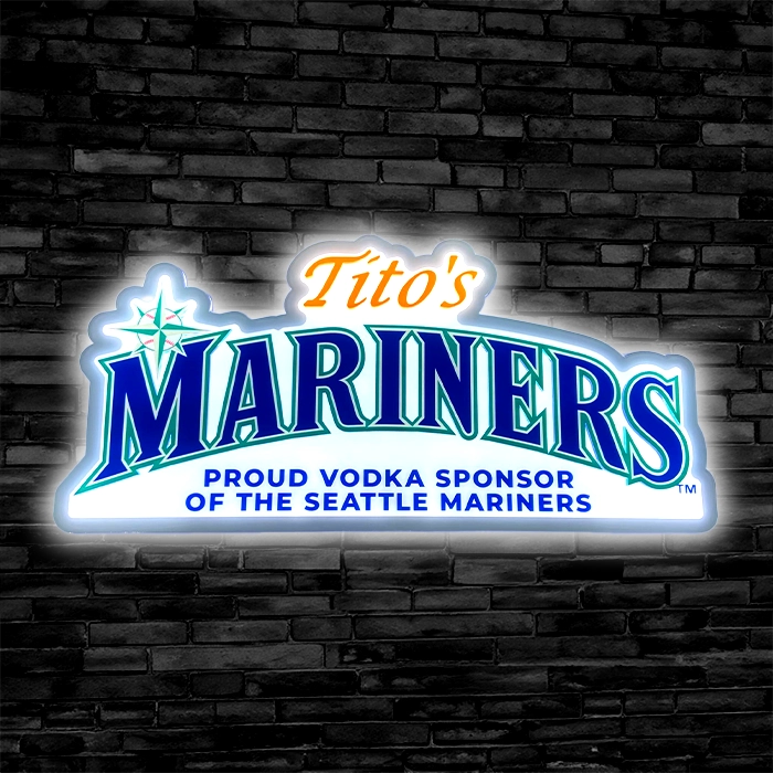 Neon sign featuring "tito's mariners" with text "proud vodka sponsor of the seattle mariners", against a dark brick wall background.