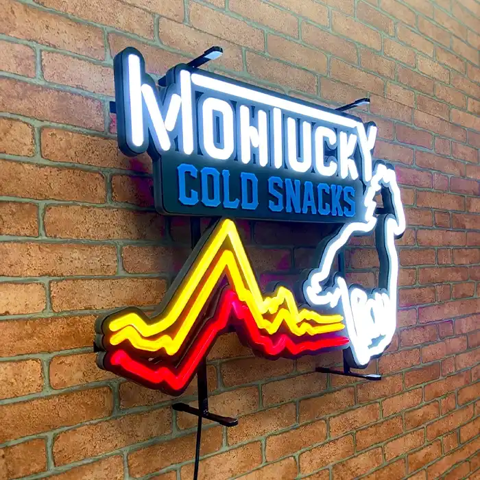 LED neon sign on a brick wall reading "montucky cold snacks" with a colorful, neon outline of a mountain and a rearing horse.
